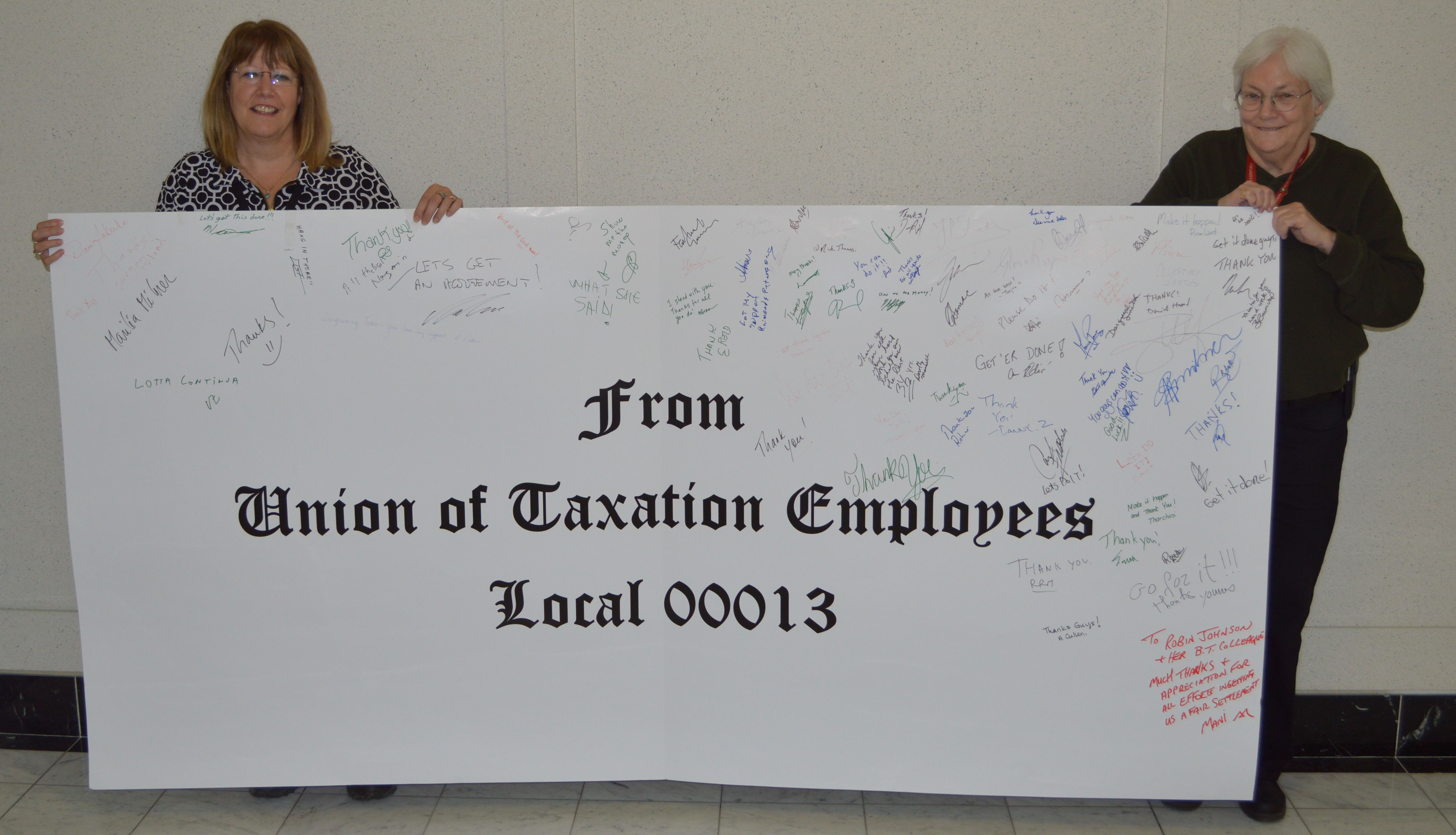 Robin Johnson and Linda Collins posing with a large card that the members signed