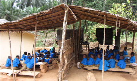 children in school uniforms sitting on benches in an outdoor school